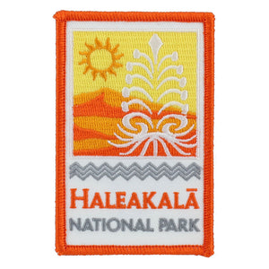 Rectangular gold, orange and white patch shows the rising sun and Haleakalā silversword over the park name: Haleakalā National Park, embroidered in orange on a white field under a kapa pattern border design.