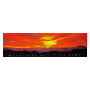 Poster is a panoramic showing the golden sunrise in an orange sky over Haleakalā volcano as seen from the summit. Clouds spill over the cliffs in the distance.