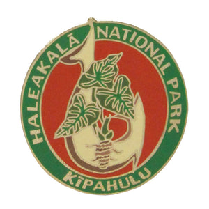 This green and red pin represents the Kīpahulu District of Haleakalā National Park, rich in Polynesian culture. The foreground of this round pin shows a fish hook, once made from shell, hardwood or bone. The taro plant, a Hawaiian staple food, is also represented. The park name, Haleakalā National Park, runs around the top 3/4 of the pin. 