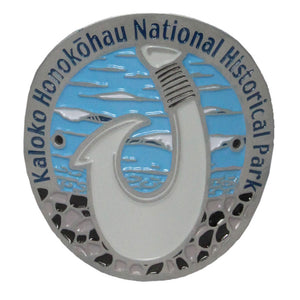 Oval pin with grey rim stating the name of the park: Kaloko-Honokōhau NHP. Pin shows a white bone traditional fish hook on a blue background representing the ocean.
